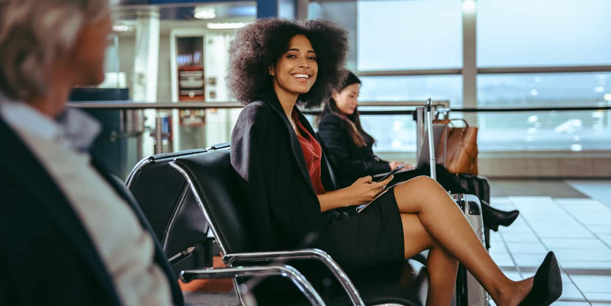 微笑的女人坐在机场拿着她的手机。